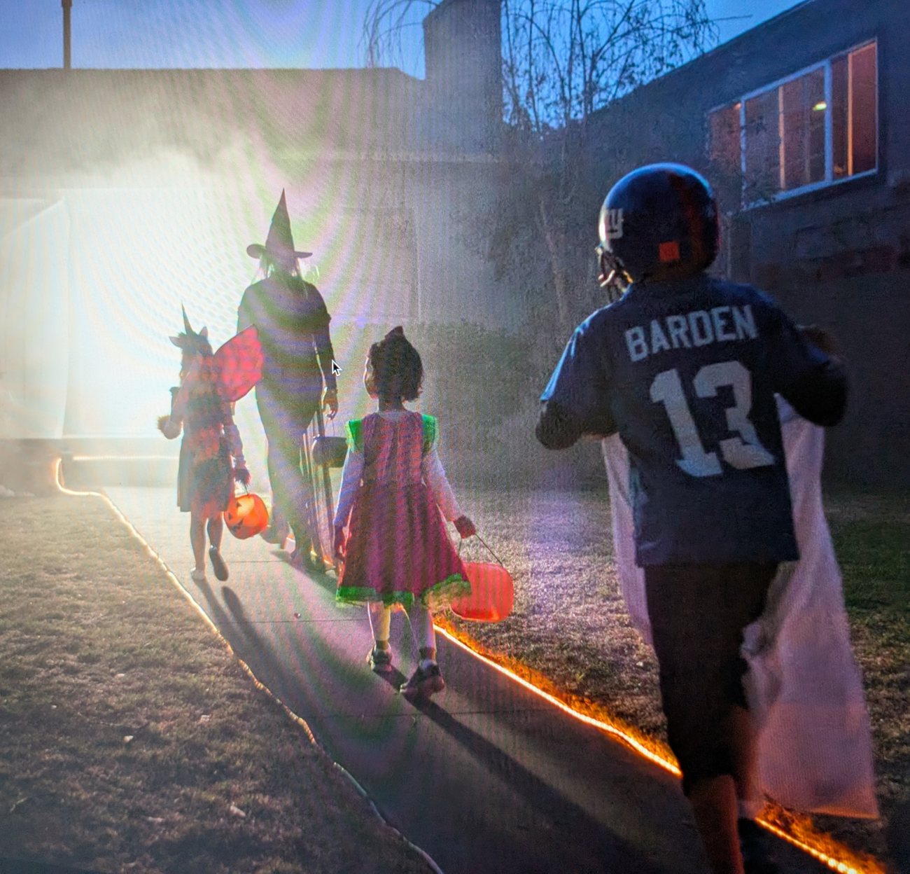 Children in Halloween costumes walking a fog-lit path toward a bright doorway