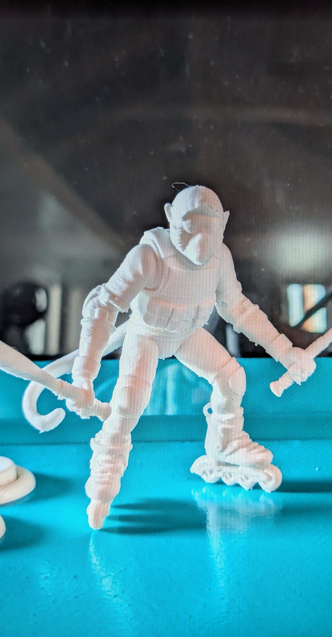White 3D-printed figure on inline skates holding two swords, on a teal air hockey table