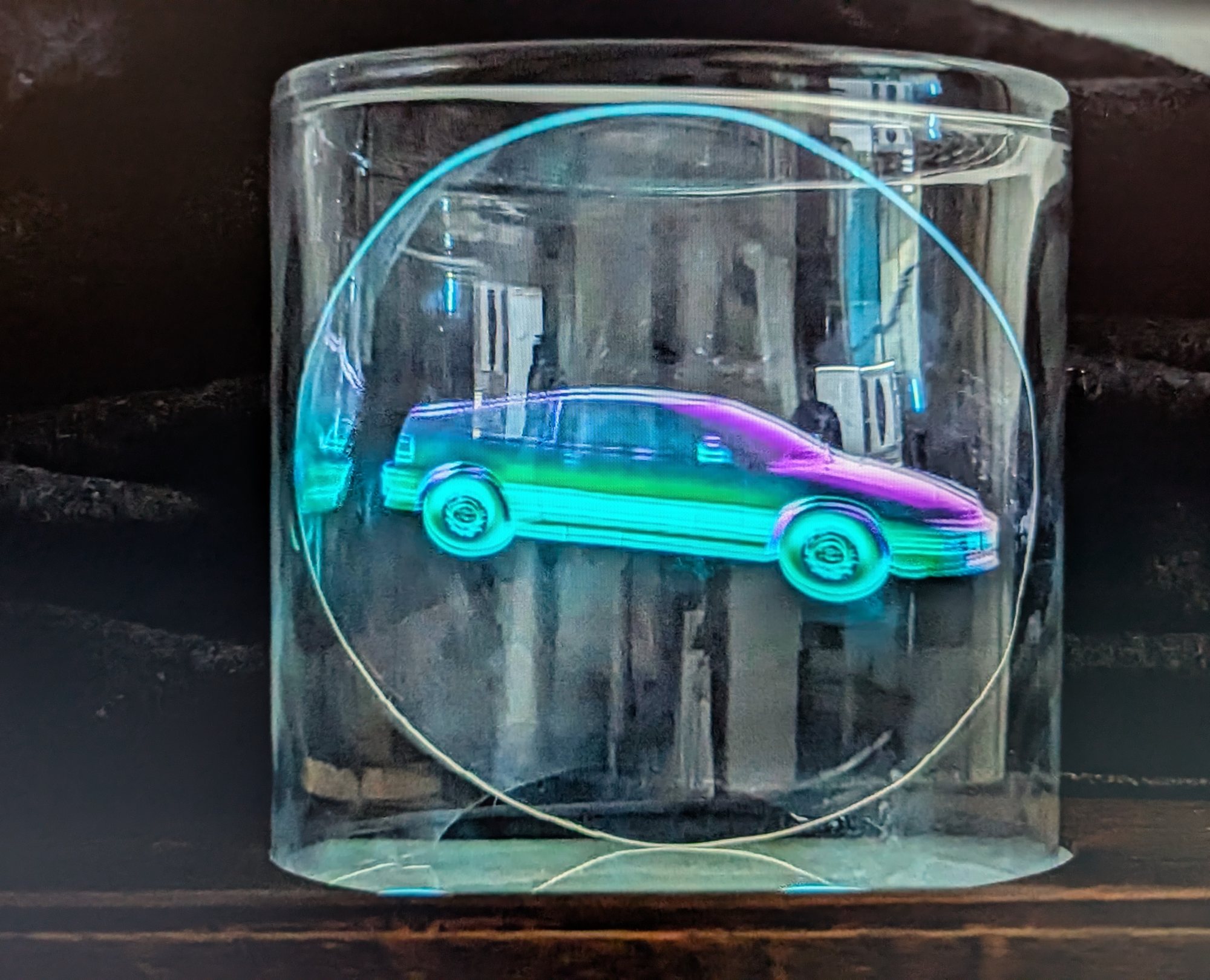 Holographic cyan and magenta car rotating inside a clear glass cylinder