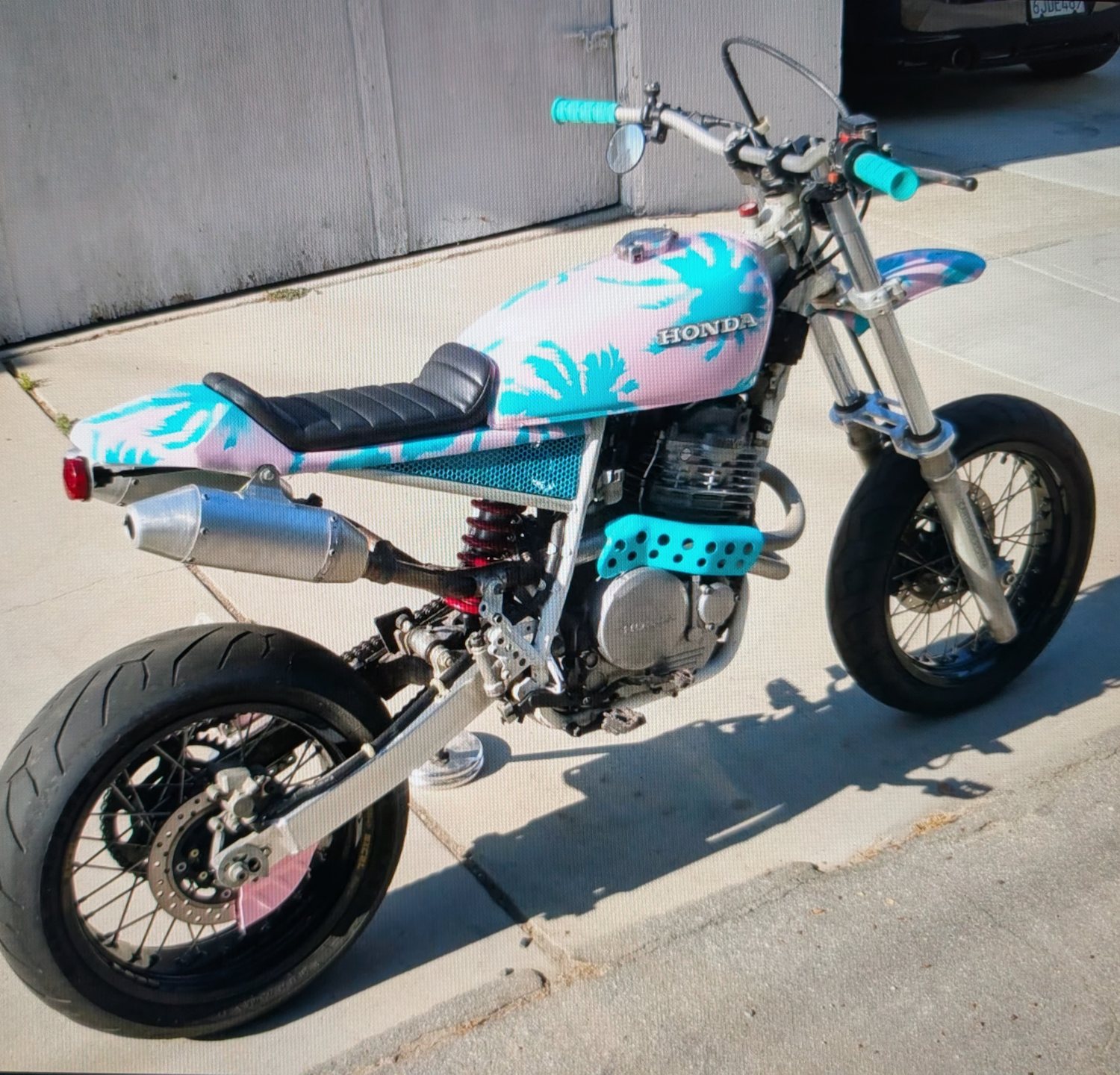 Honda supermoto with a pink and teal palm-print tank and matching grips